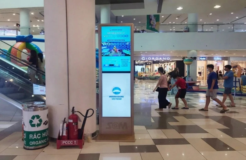 Minh họa LCD/LED tại trung tâm thương mại: Digital poster trong sảnh với khách đi qua phía sau