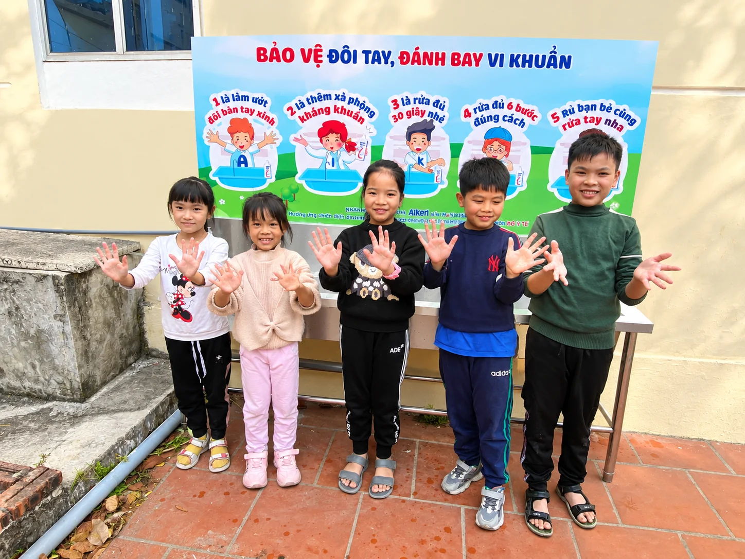 Aiken — Các em nhỏ cùng lan tỏa thông điệp rửa tay trước bảng nhận diện Aiken